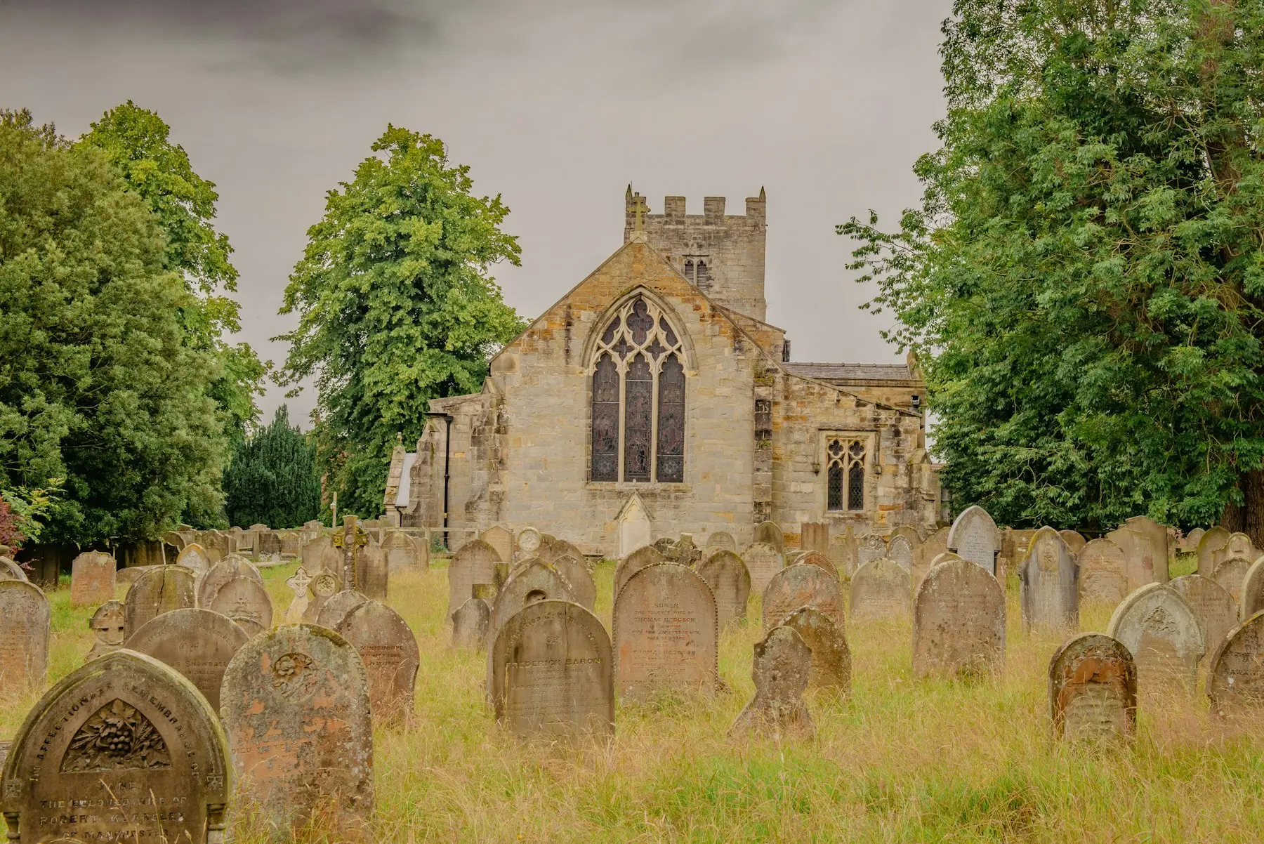 Weathered gravestones in long grass beside a medieval English church.