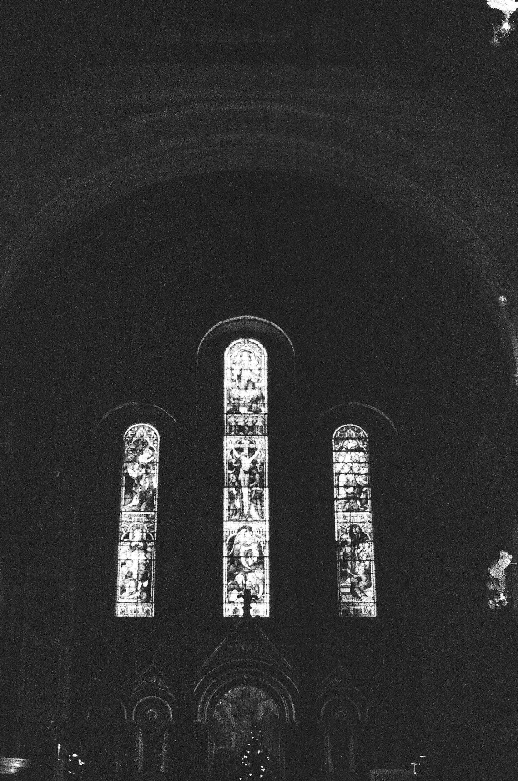 Three pointed Gothic windows emerging from the dark interior of a church.